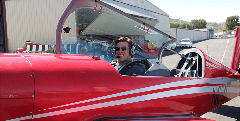 Brandon sitting in the cockpit of a red plane ready to fly the plane